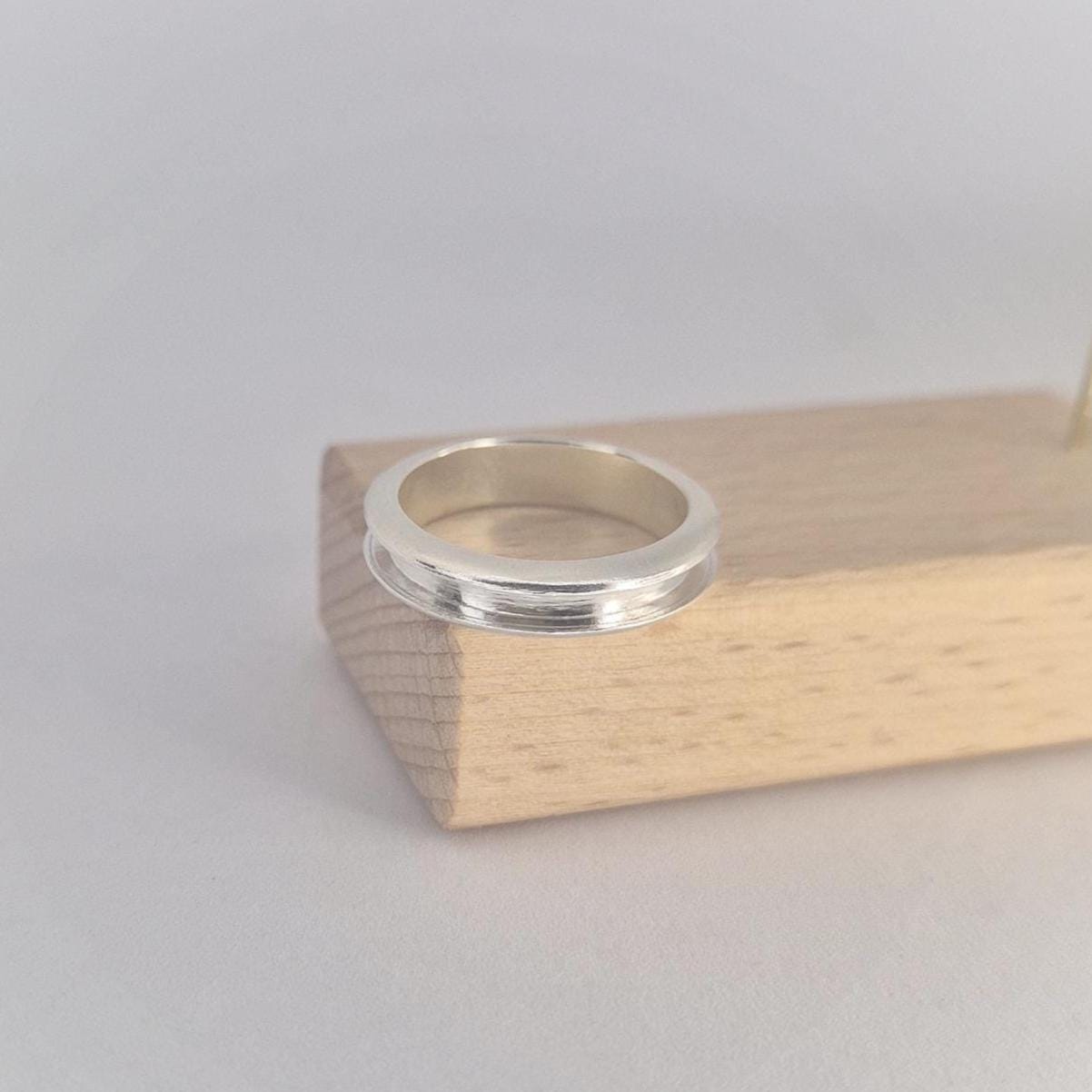 Minimalist silver channel band resting flat on a light wood block, showing the smooth polished outer surface and slim proportions.