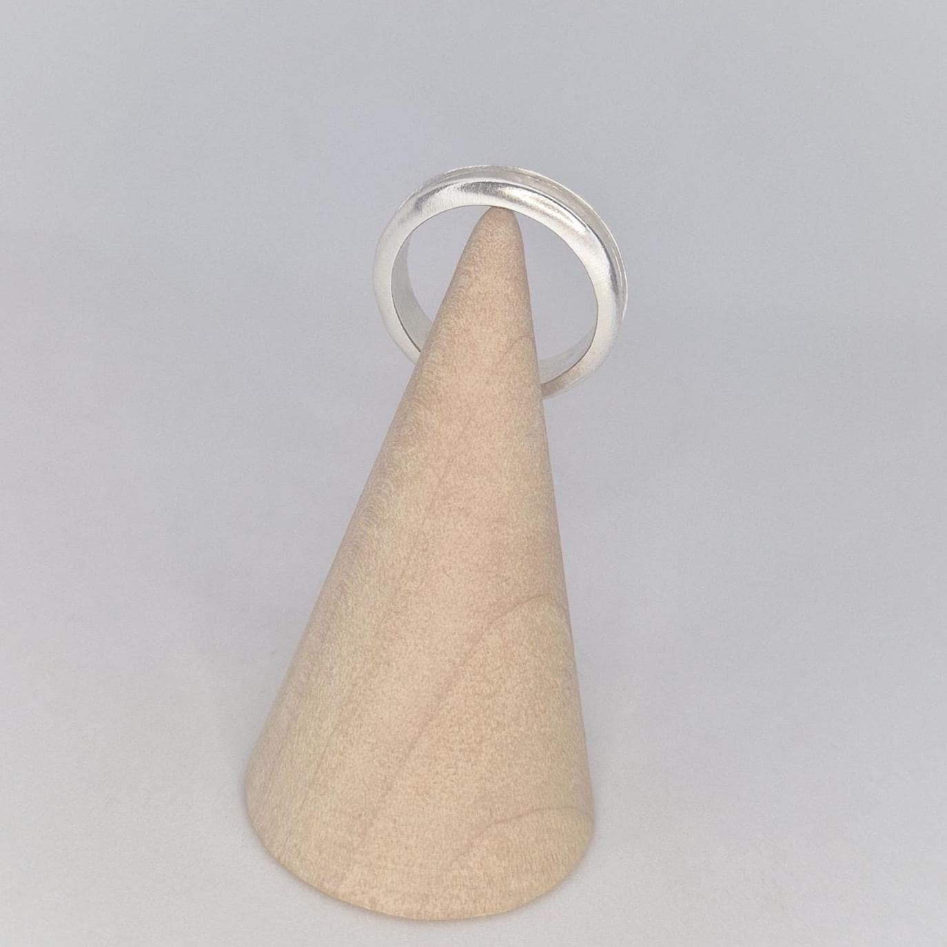 Angled view of a narrow silver channel ring on a wooden cone, showing the subtle groove detail running around the band.