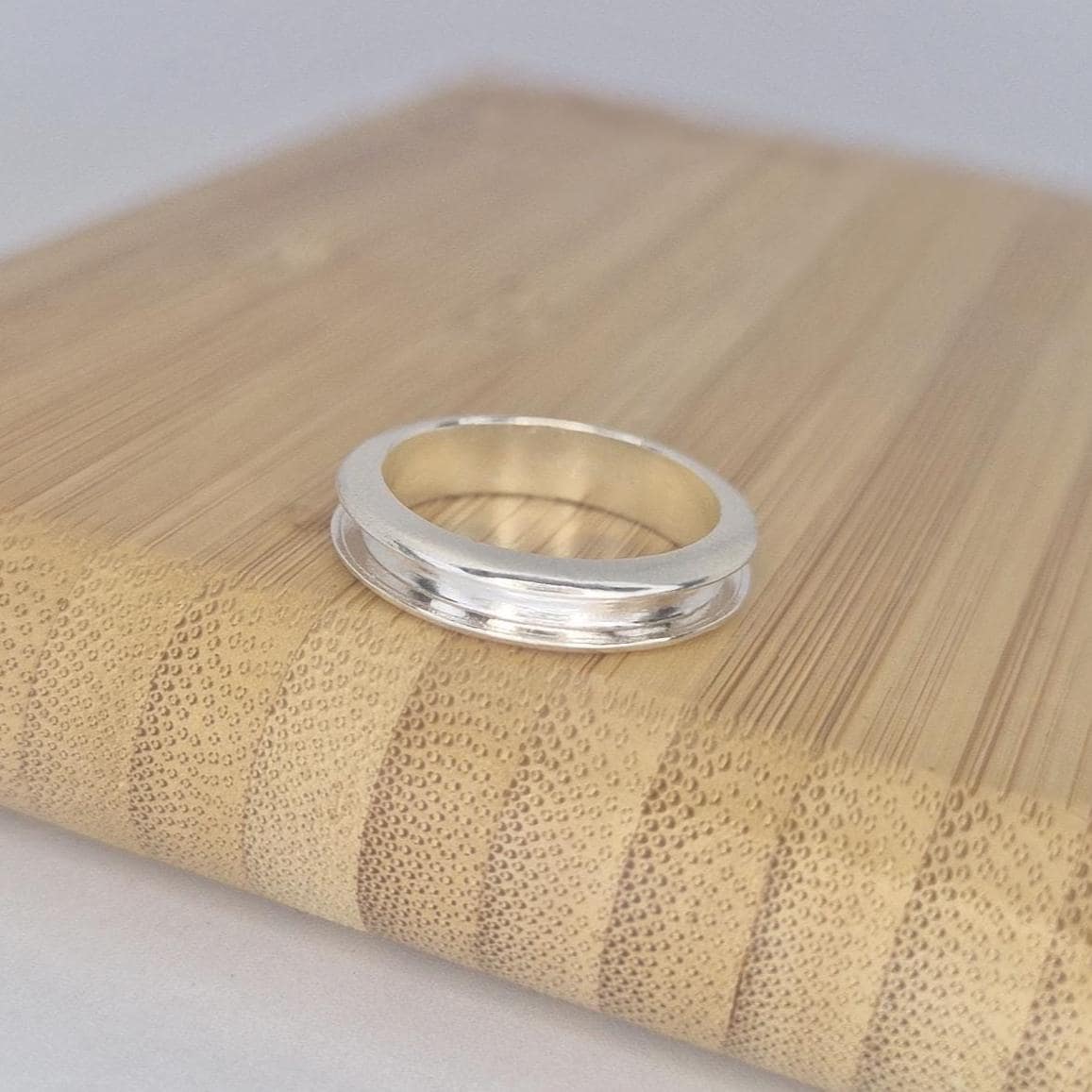 Polished silver channel ring resting on a bamboo block, photographed from above to show the smooth inner band and refined craftsmanship.