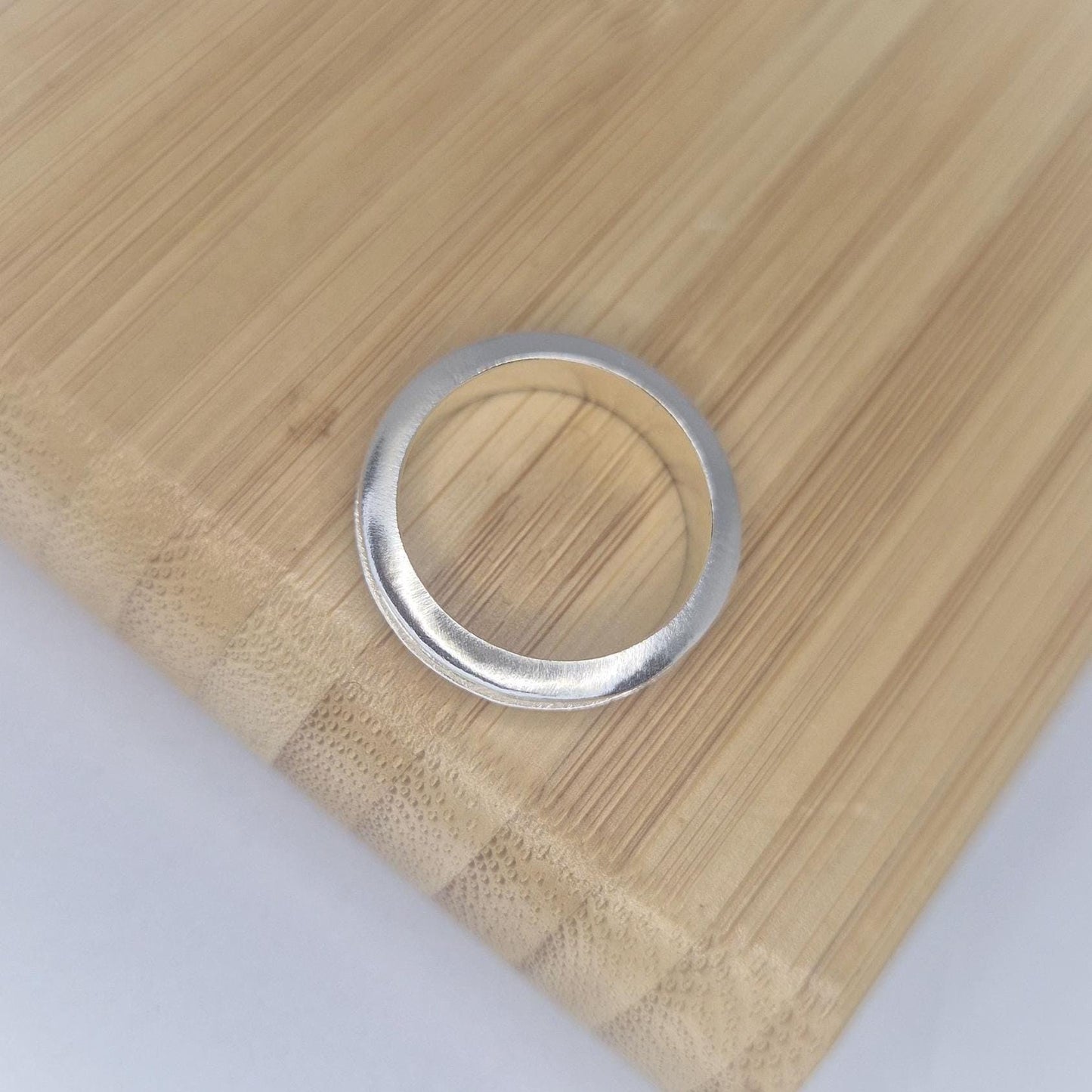 Top-down view of a slim silver channel ring on a bamboo surface, highlighting the curved outer profile and minimalist design.
