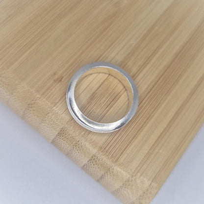 Top-down view of a slim silver channel ring on a bamboo surface, highlighting the curved outer profile and minimalist design.
