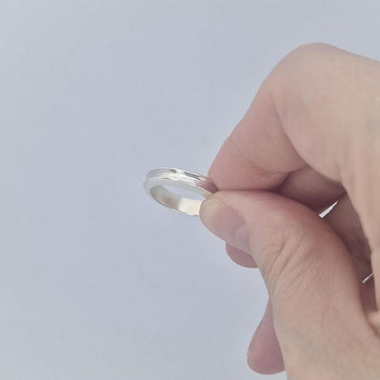 Hand holding a slim silver channel ring between fingers, showing the lightweight feel and smooth polished finish.