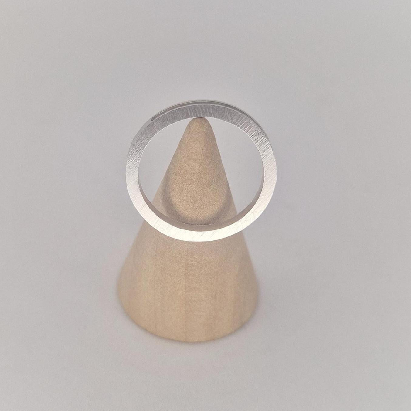 Front view of a very slim silver 120° channel ring displayed on a wooden cone stand against a soft white background.
