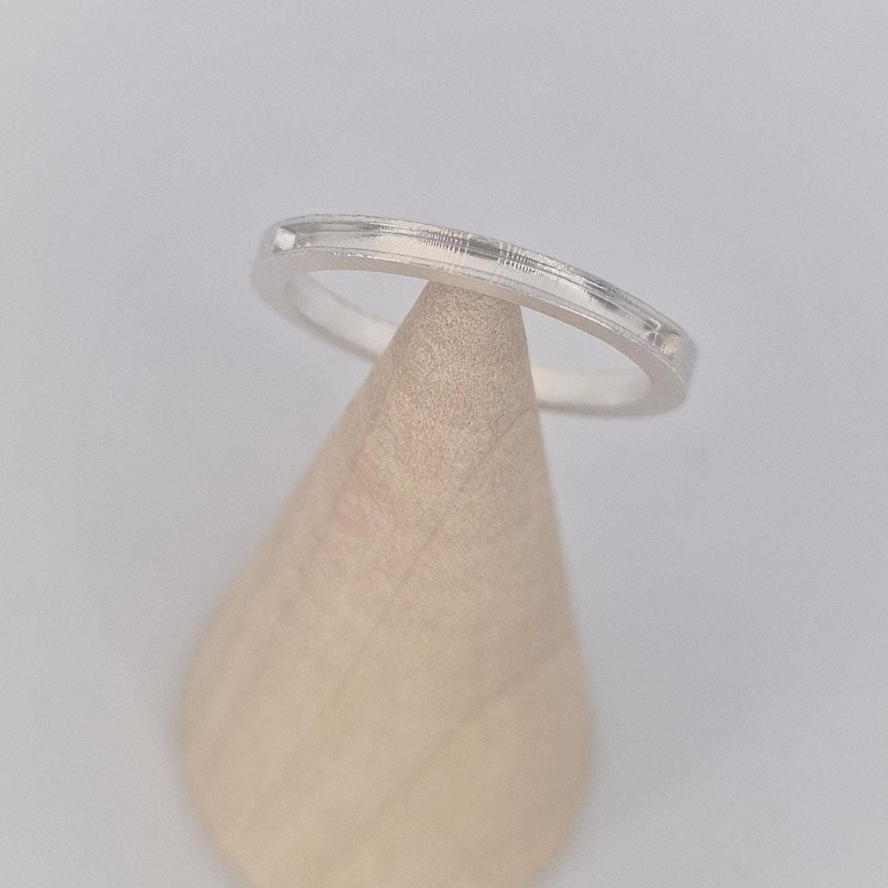 Angled close-up of a slim silver 120° channel ring on a wooden cone, emphasising the subtle channel cut and refined edge profile.