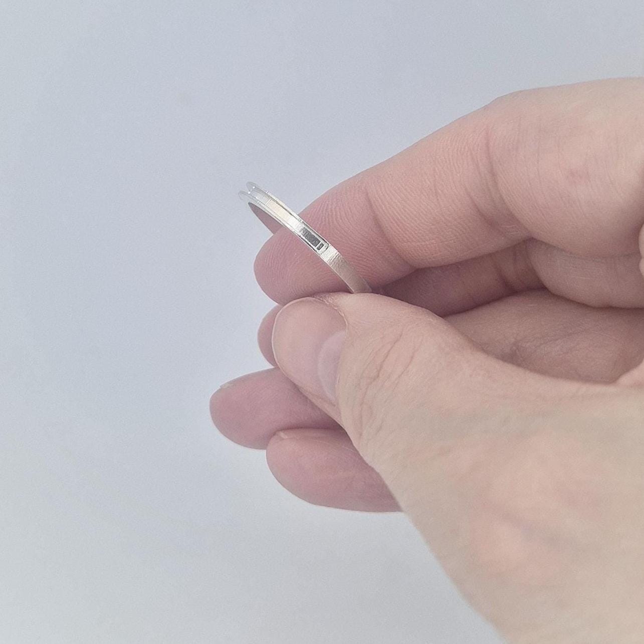 Hand holding a very slim silver 120° channel ring between fingers, showing the delicate thickness and polished finish.