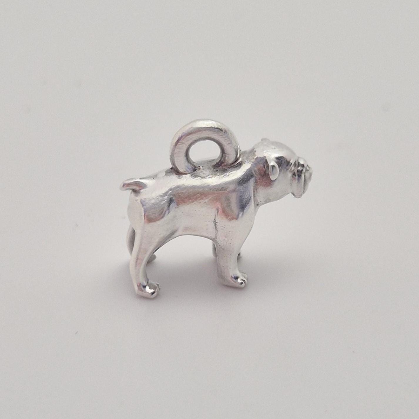 Rear three-quarter view of a solid silver bulldog charm, showing the muscular body and smooth polished finish.