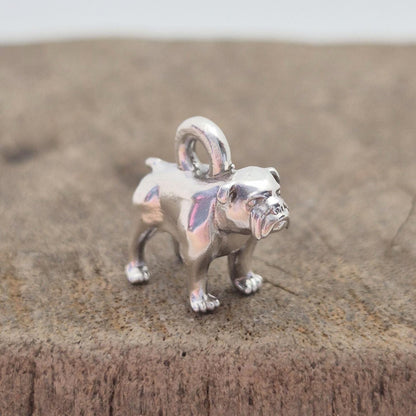 Angled side view of a silver bulldog charm on wood, showing the body shape and rounded top loop for attaching to chains or bracelets.