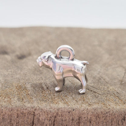 Profile view of a silver bulldog charm standing on a wooden surface, showing leg stance and solid cast form.