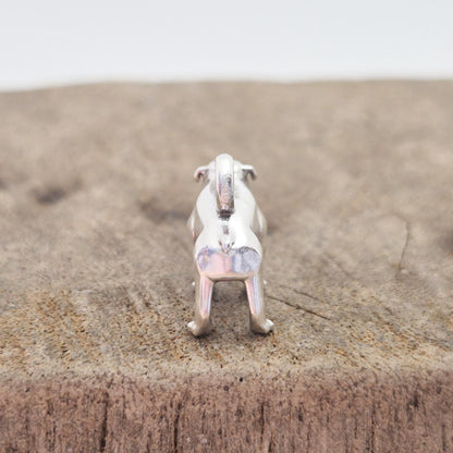 Rear view of a silver bulldog charm on wood, highlighting the proportions, tail, and polished metal surface.