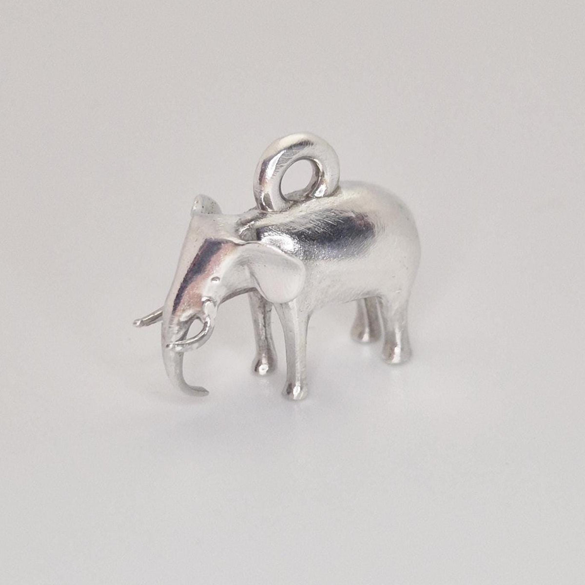 Angled side view of a silver elephant charm, showing the raised trunk, tusk detail, and rounded body shape.