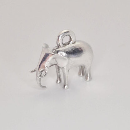 Angled side view of a silver elephant charm, showing the raised trunk, tusk detail, and rounded body shape.