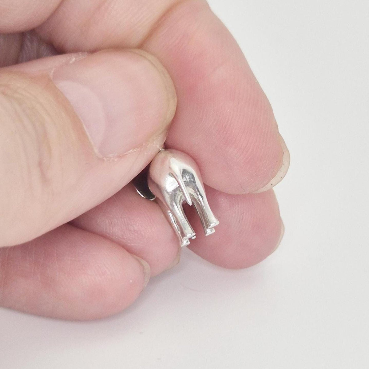Close-up rear view of a silver elephant charm held between fingers, highlighting the tail and back leg detail.