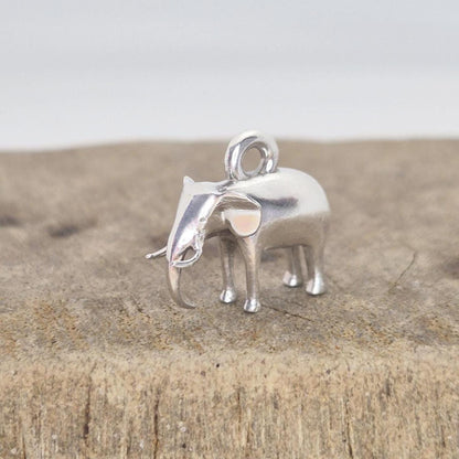 Silver elephant charm displayed on a wooden surface, photographed from the side to show scale and surface texture contrast.