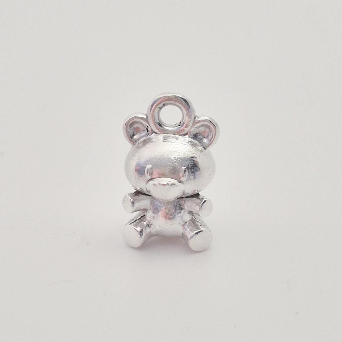 Front view of solid silver teddy bear charm with rounded ears and seated pose, polished finish