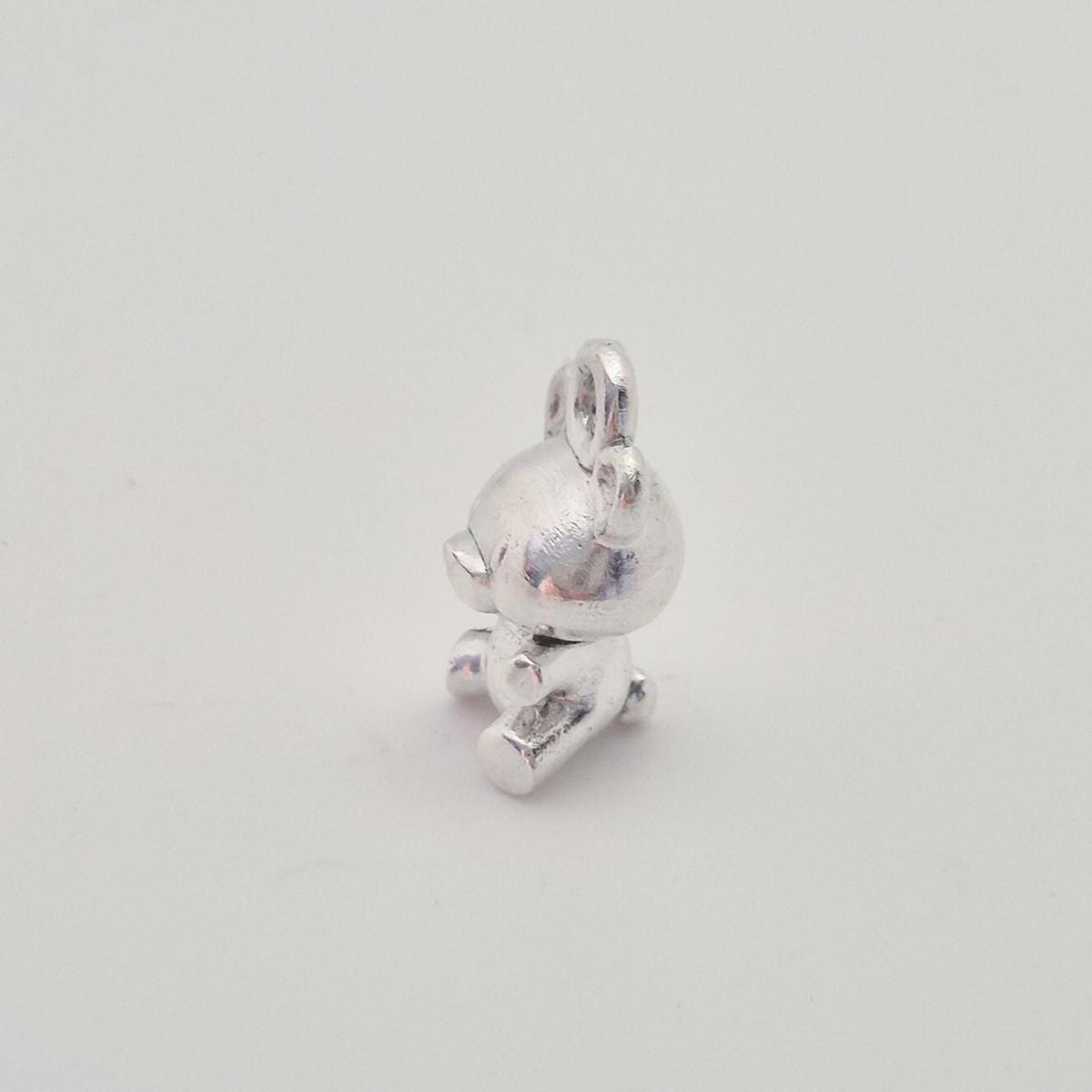 Side view of silver teddy bear charm showing bail loop and sculpted arms and legs