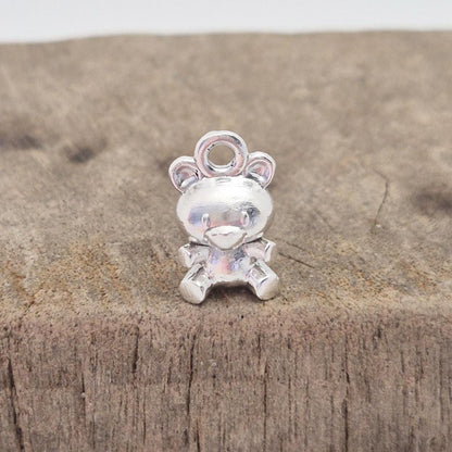 Close-up of front of silver teddy bear charm showing facial features and polished finish