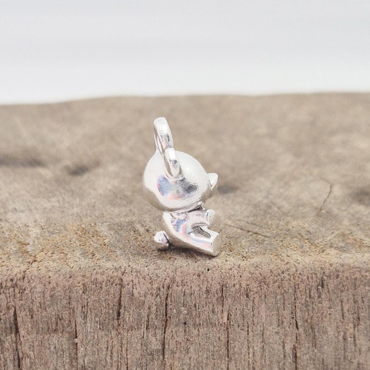 Side view of silver teddy bear charm on wooden surface showing depth and bail orientation