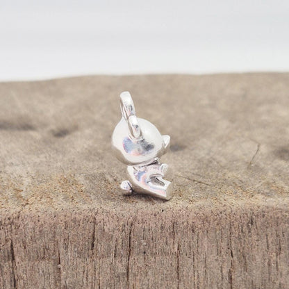 Side view of silver teddy bear charm on wooden surface showing depth and bail orientation