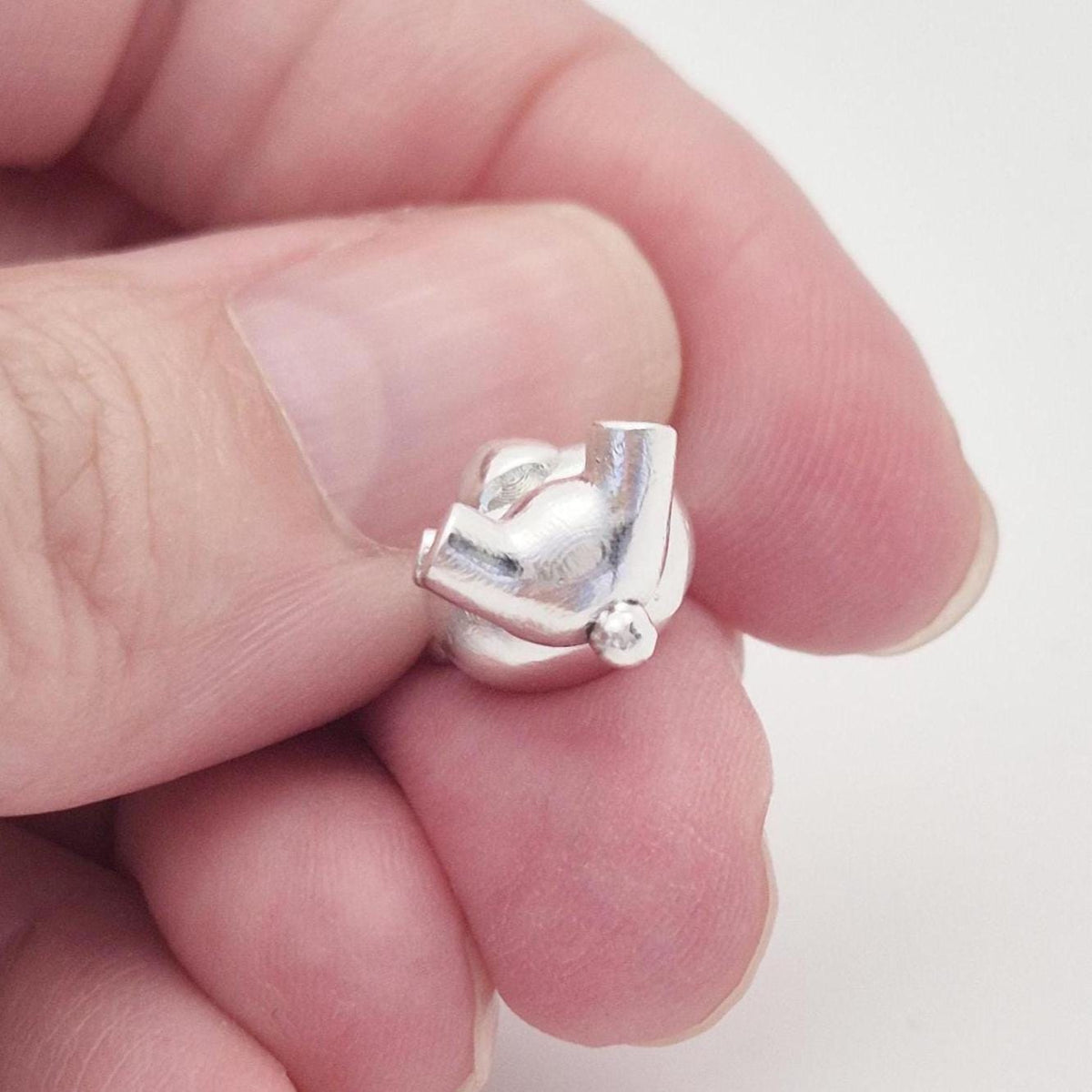 Bottom view of silver teddy bear charm held in hand to show scale