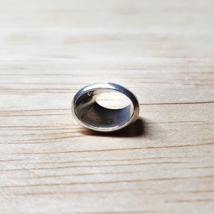 Oval 6x4mm silver bezel lying on its side on a light wood background, showing the interior cavity for a gemstone