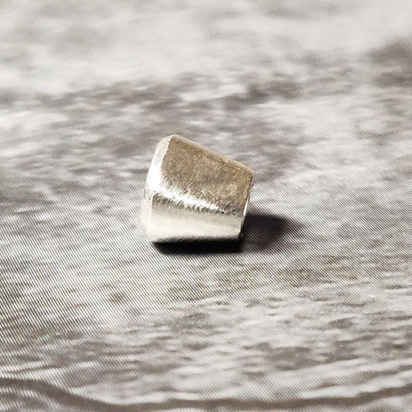 Small oval 6x4mm silver bezel setting photographed on a dark textured background, showing the tapered sides.