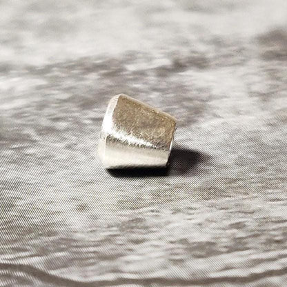 Small oval 6x4mm silver bezel setting photographed on a dark textured background, showing the tapered sides.