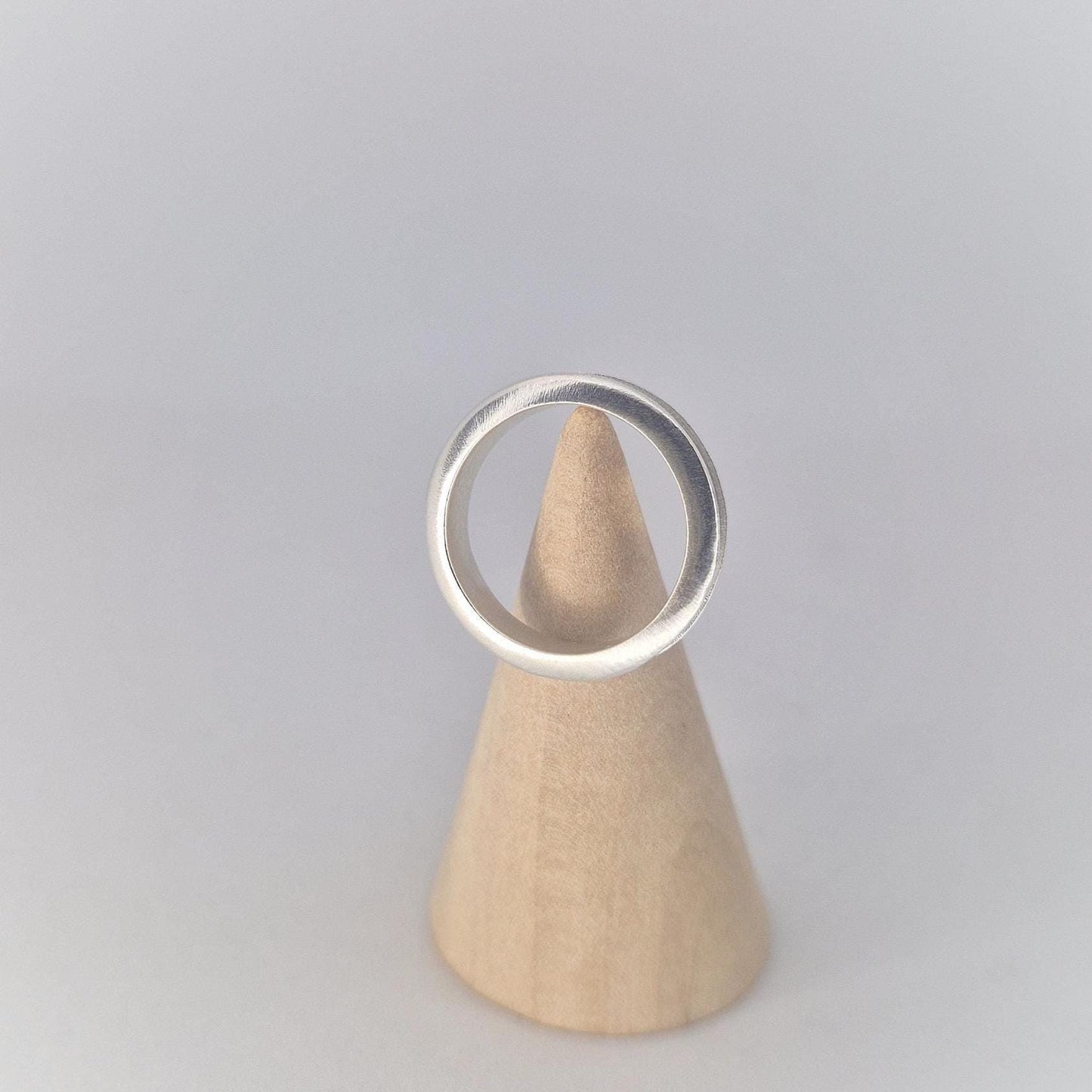 Front view of a slim silver channel ring displayed on a wooden cone stand, highlighting the gently rounded profile and clean modern design.
