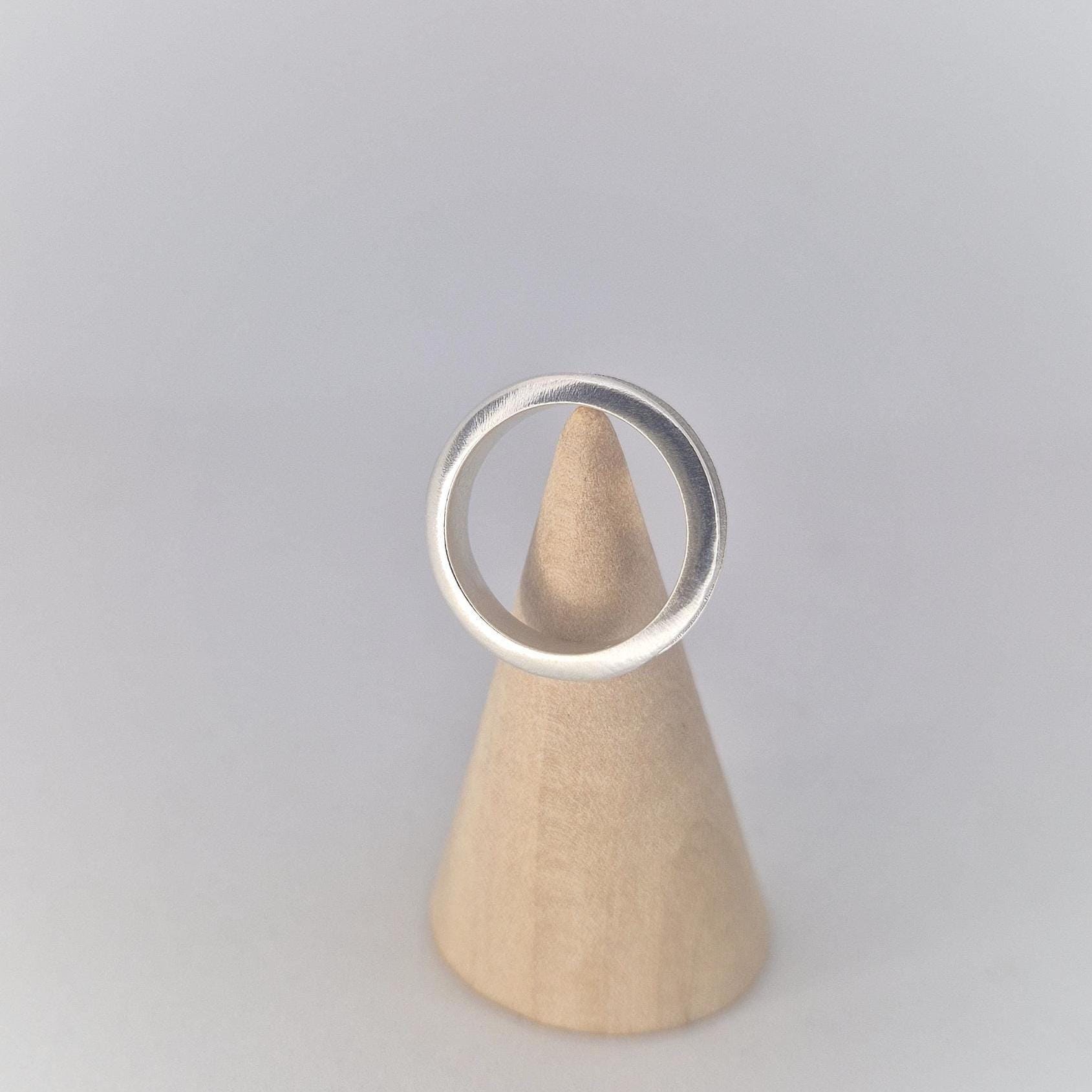 Front view of a slim silver channel ring displayed on a wooden cone stand, highlighting the gently rounded profile and clean modern design.