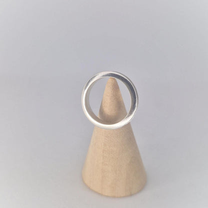 Front view of a slim silver channel ring displayed on a wooden cone stand, highlighting the gently rounded profile and clean modern design.