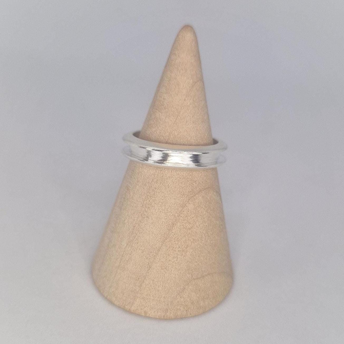 Side profile of a slim silver channel band on a wooden cone stand, emphasising the curved edges and polished finish.