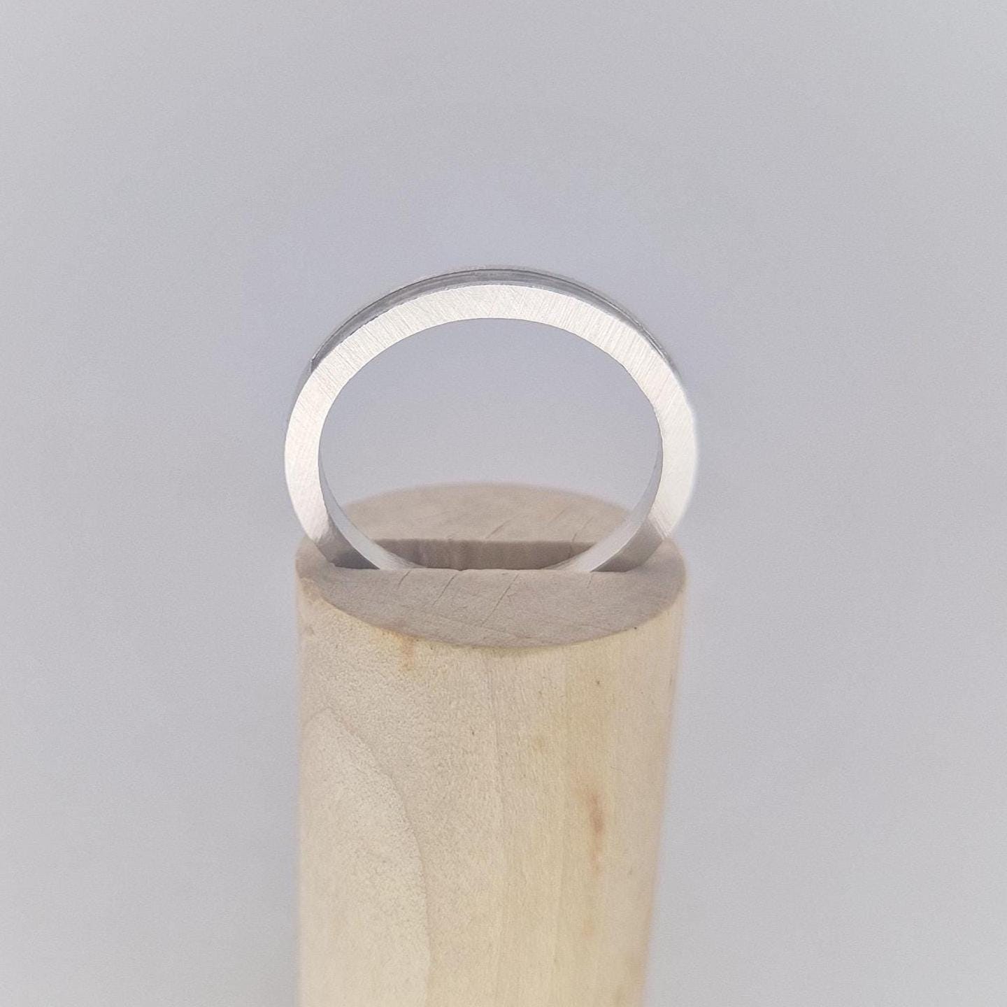 Straight-on view of a very slim silver 120° channel ring resting on a cylindrical wooden display, highlighting its minimalist design.