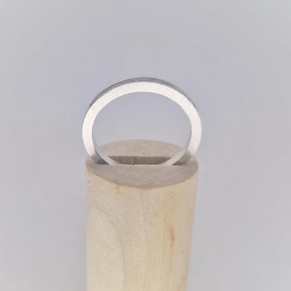 Straight-on view of a very slim silver 120° channel ring resting on a cylindrical wooden display, highlighting its minimalist design.