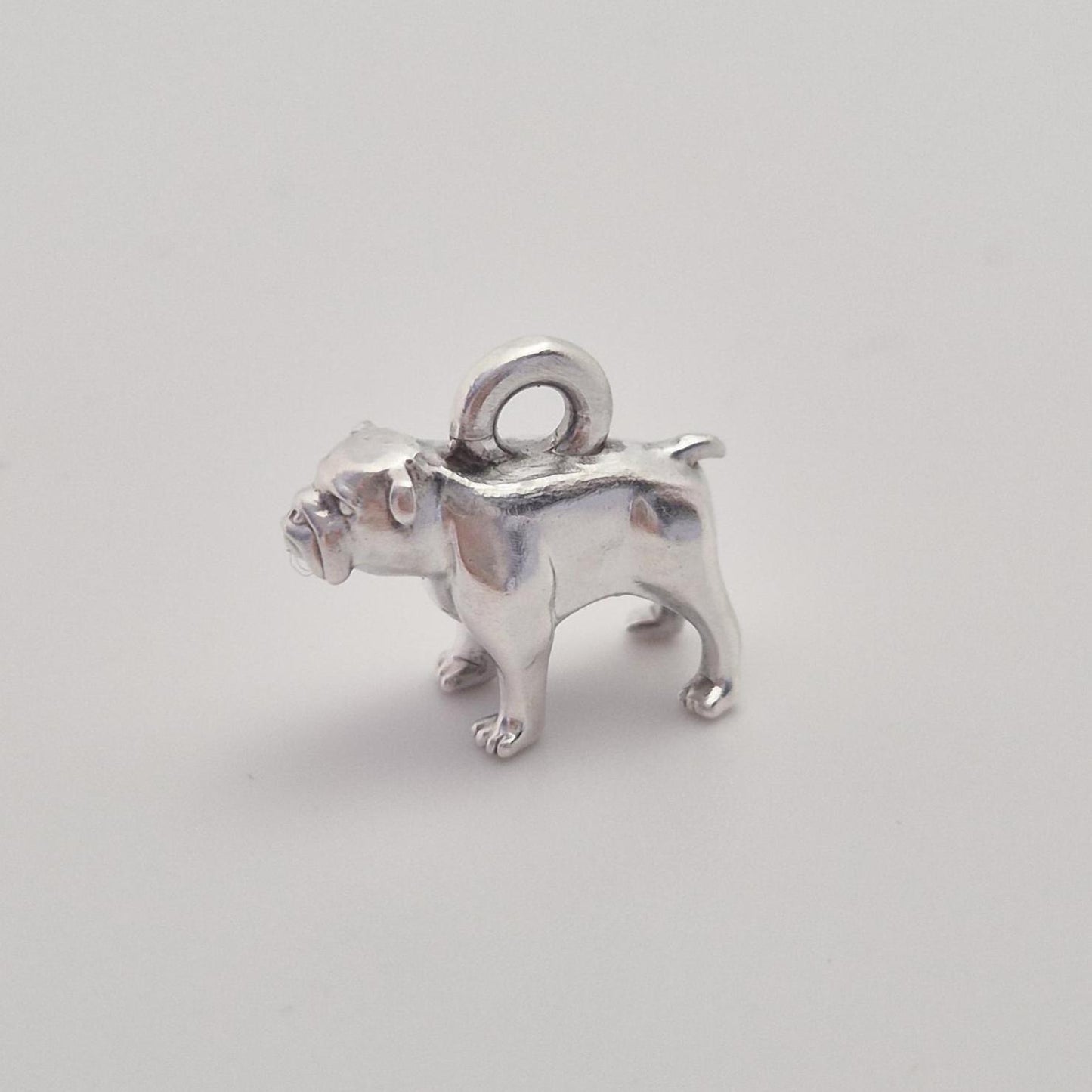 Side view of a silver bulldog charm with integrated top loop, photographed against a clean white background.