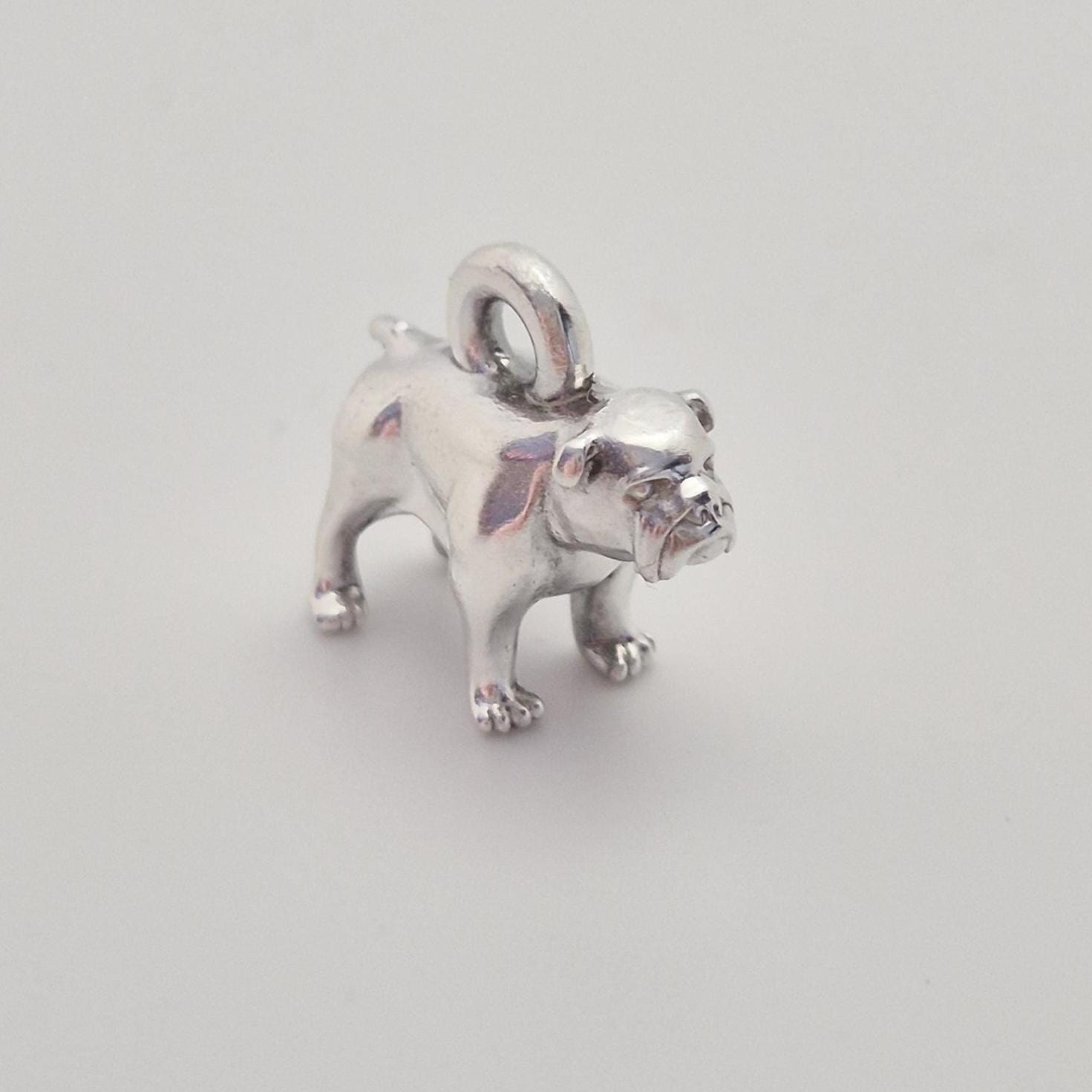 Angled front view of a silver bulldog charm on a white background, emphasising the expressive facial details and compact proportions.