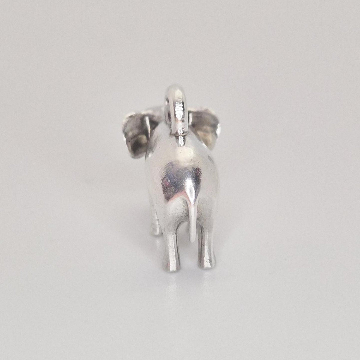 Rear view of a silver elephant charm against a white background, highlighting the tail, back legs, and smooth cast finish.
