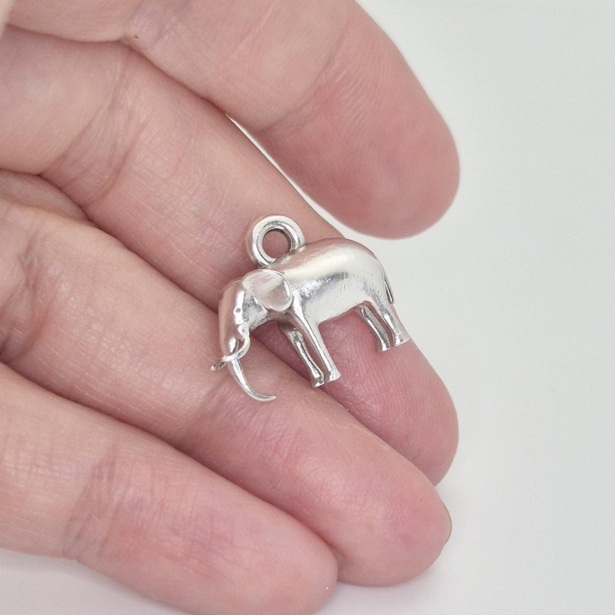 Silver elephant charm held between fingers to show scale, thickness, and integrated hanging loop.