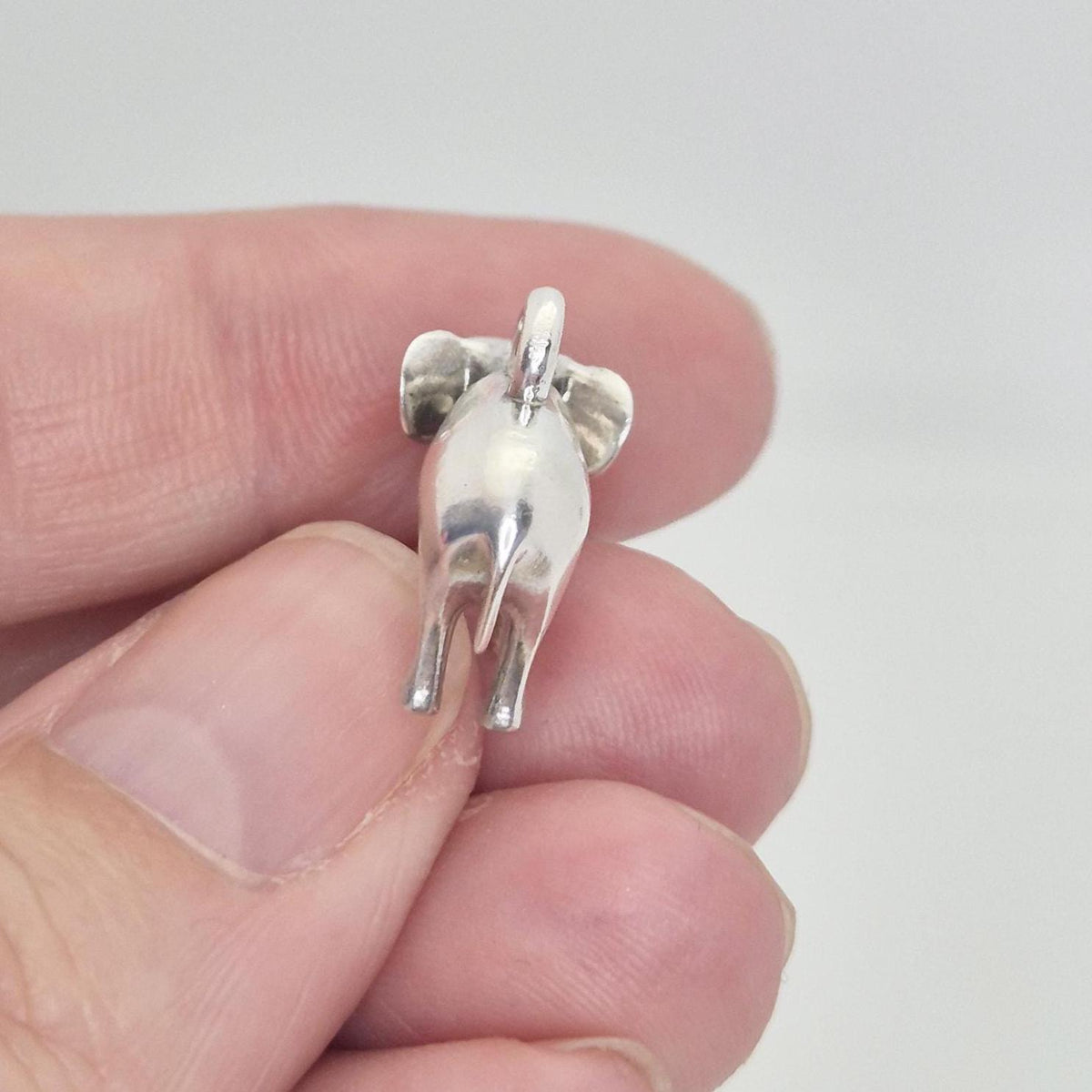 Close-up rear view of a silver elephant charm held between fingers, highlighting the tail and back leg detail.