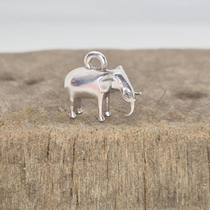 Silver elephant charm displayed on a wooden surface, photographed from the side to show scale and surface texture contrast.