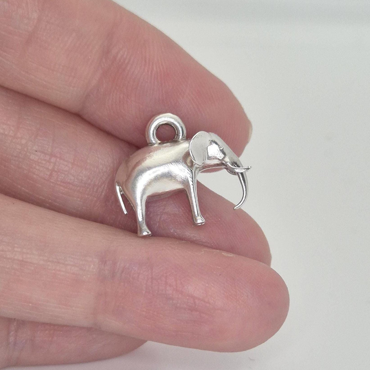 Silver elephant charm held between fingers to show scale, thickness, and integrated hanging loop.