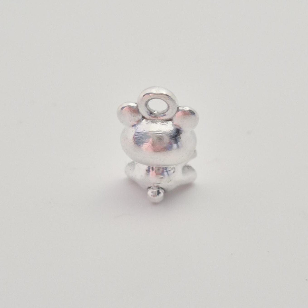 Rear view of small silver teddy bear charm highlighting smooth back and polished surface