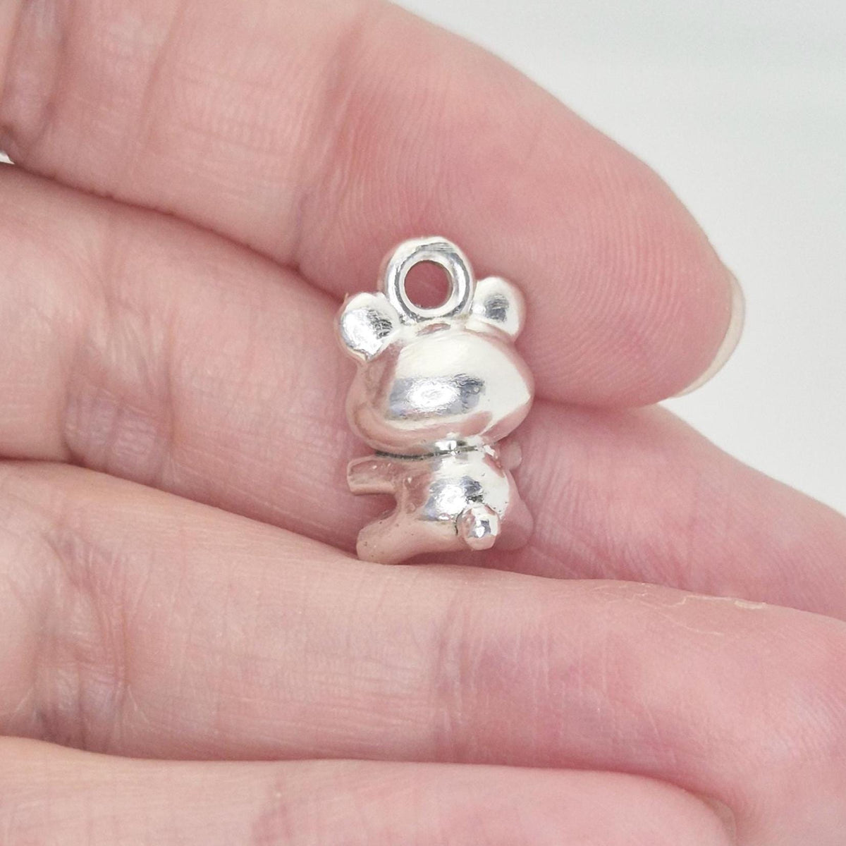 Rear view of silver teddy bear charm held between fingers to show scale and three-dimensional form