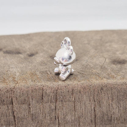 Silver teddy bear charm displayed on wooden surface for texture contrast
