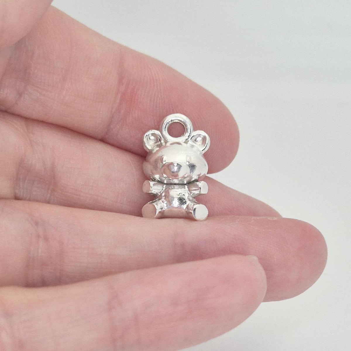 Silver teddy bear charm held between fingers to show scale and three-dimensional form