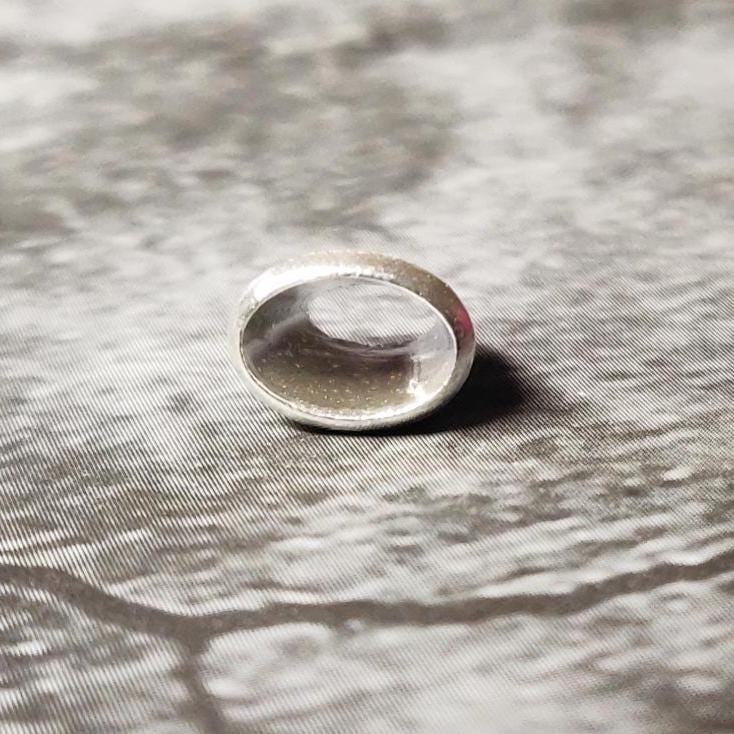 Upright 6x4mm oval silver bezel setting on a dark surface, showing the clean rim and inner seat for an oval stone.