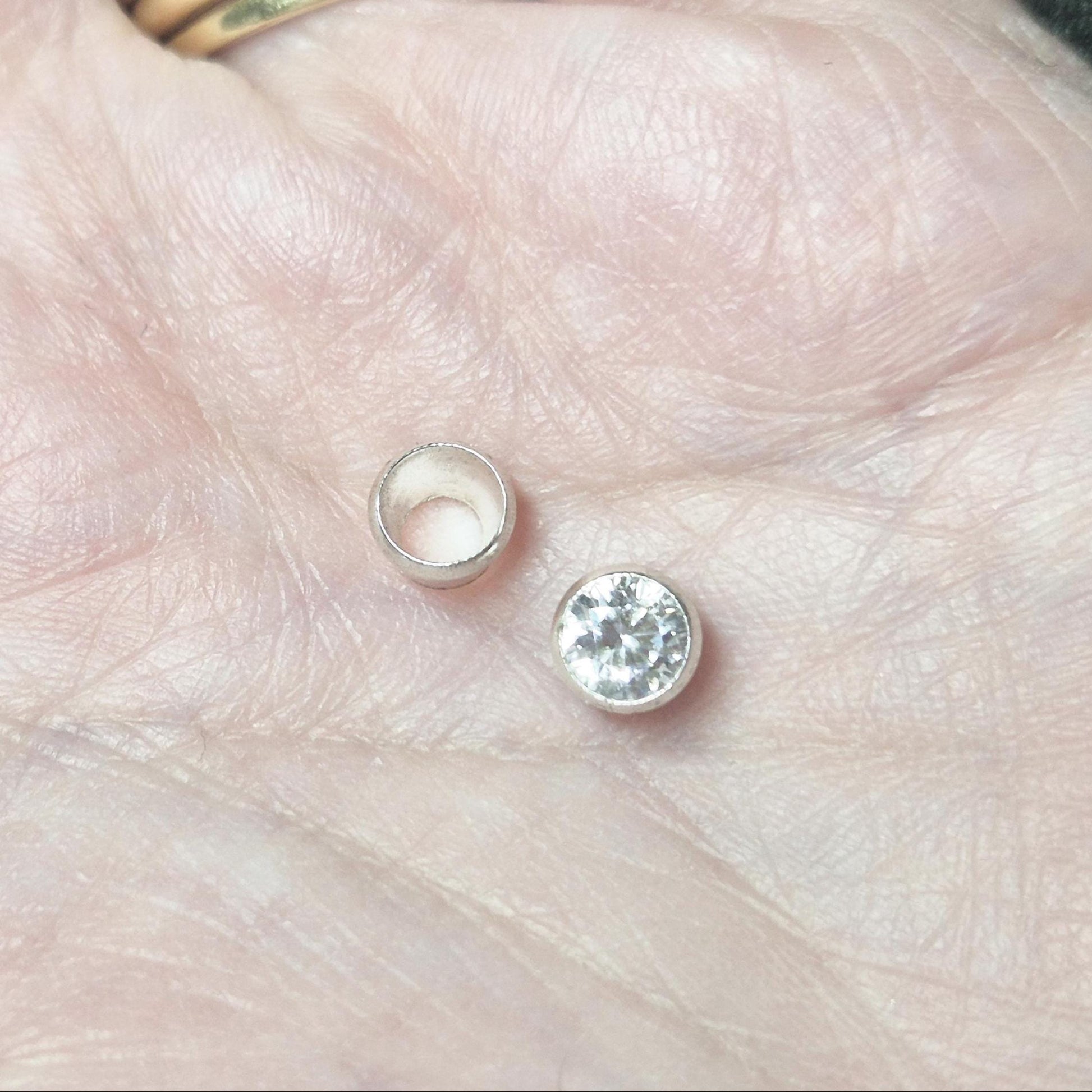 Sterling silver round bezel cup and matching gemstone shown in hand for scale, jewellery bezel setting component.