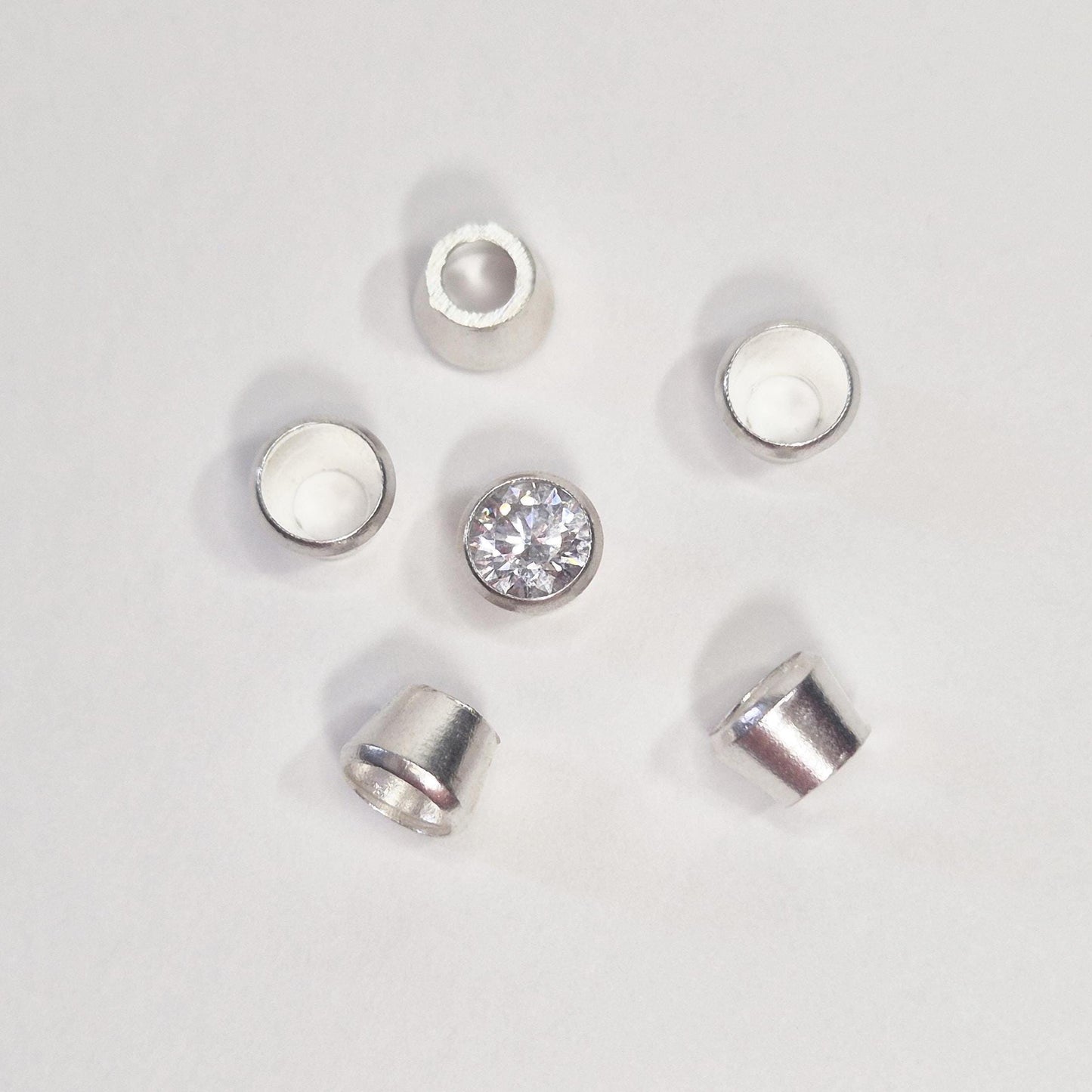 Arrangement of sterling silver bezel cups surrounding a round gemstone, showing tapered bezel settings for jewellery making.