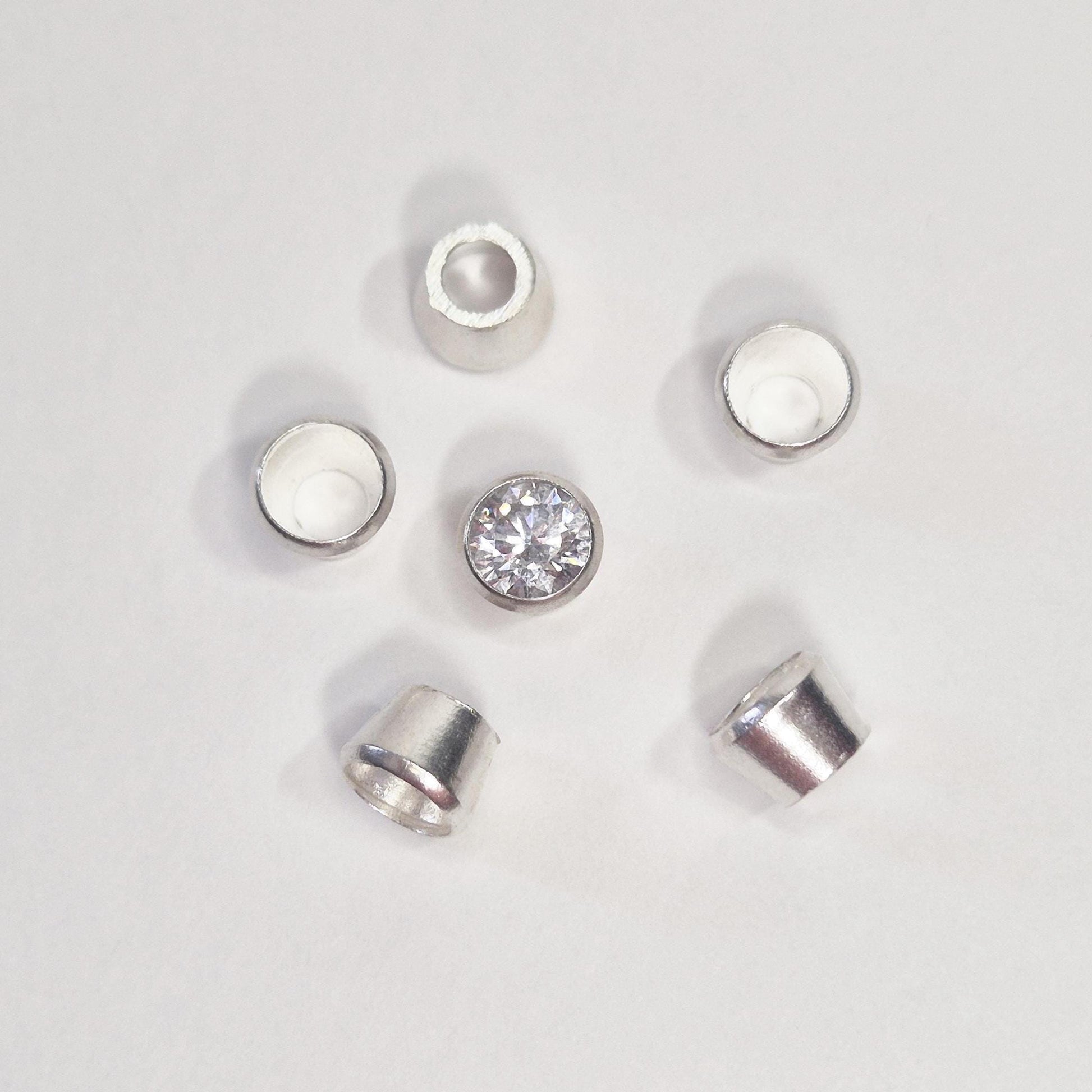Arrangement of sterling silver bezel cups surrounding a round gemstone, showing tapered bezel settings for jewellery making.