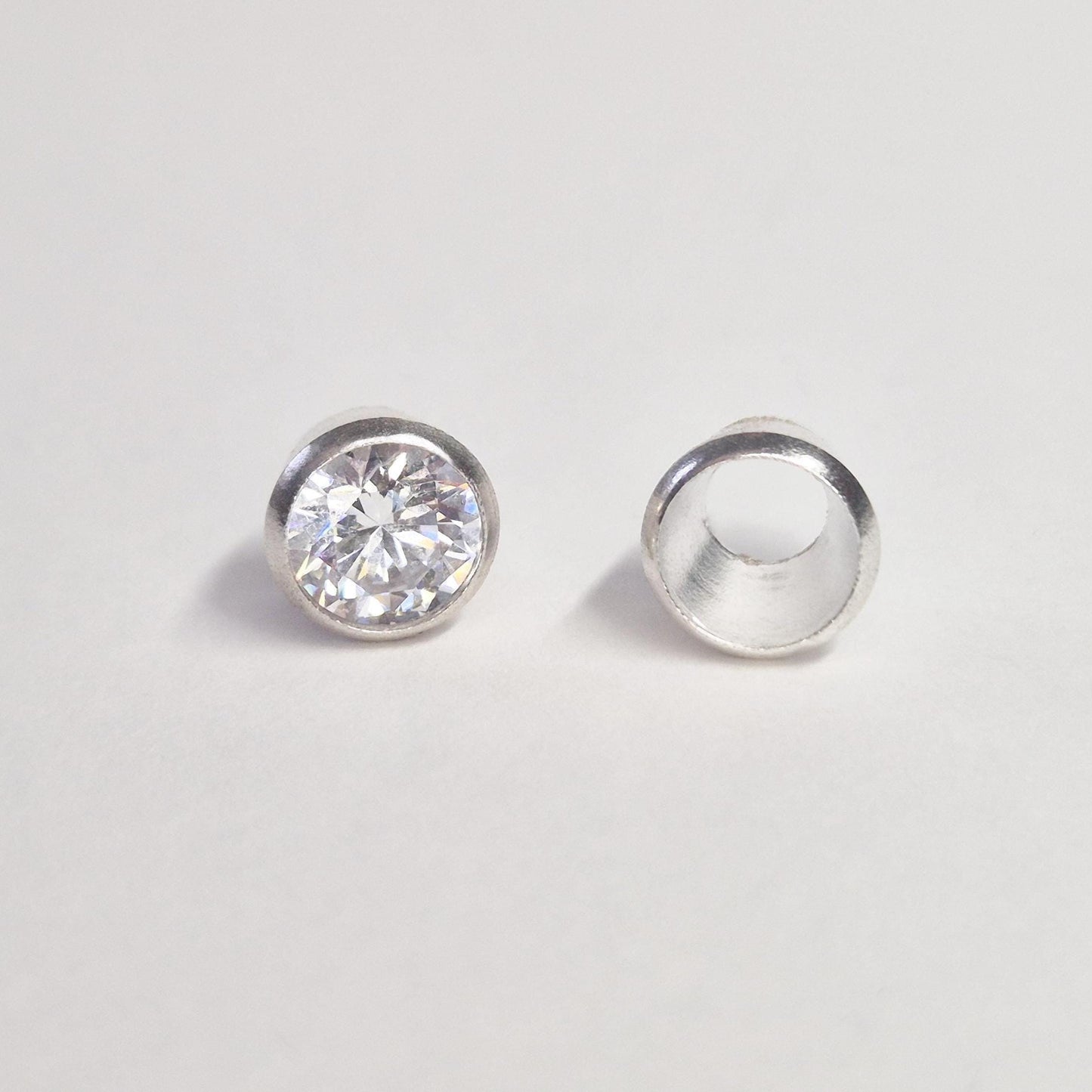 Finished round gemstone set in sterling silver bezel beside empty bezel cup, jewellery setting component on white background.