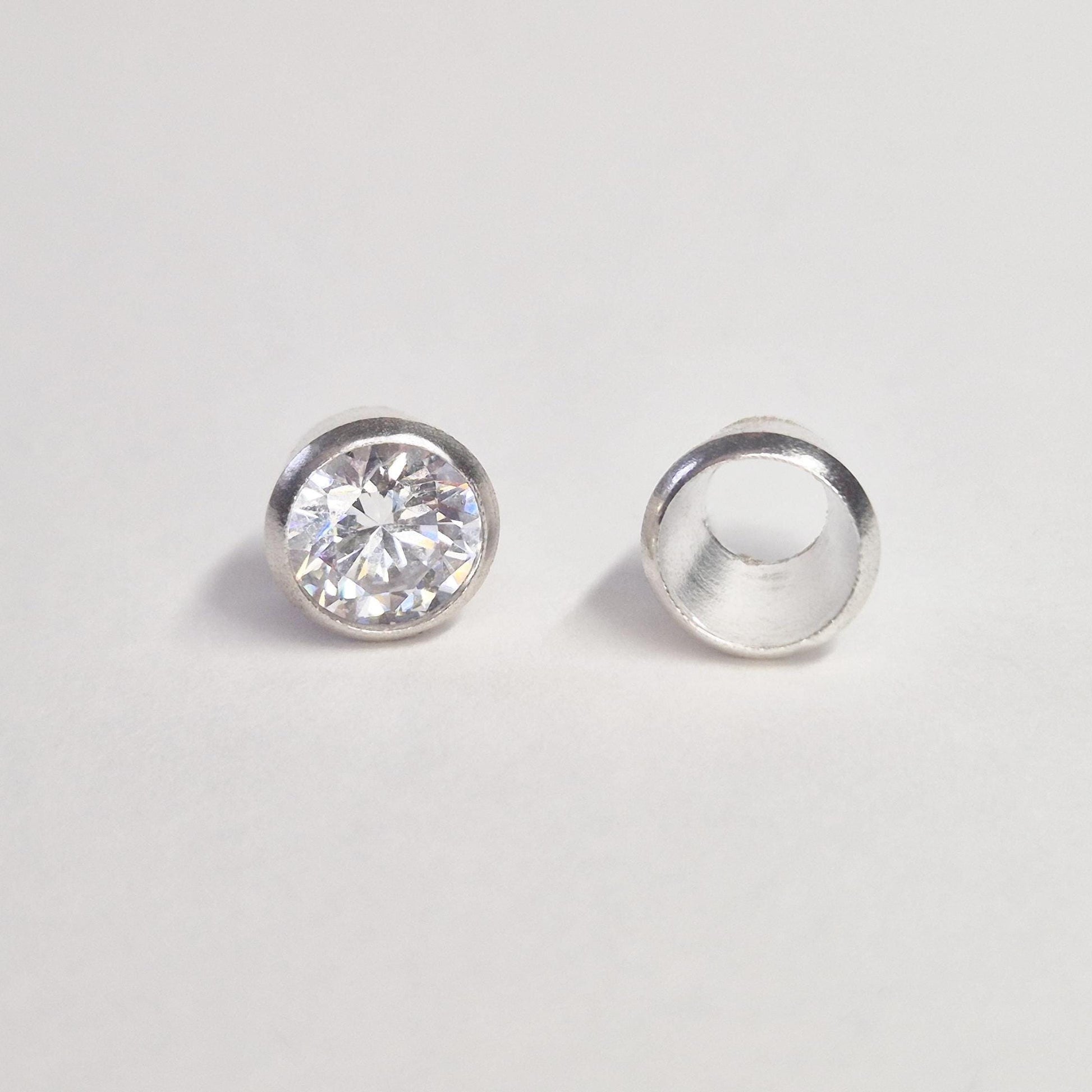 Finished round gemstone set in sterling silver bezel beside empty bezel cup, jewellery setting component on white background.