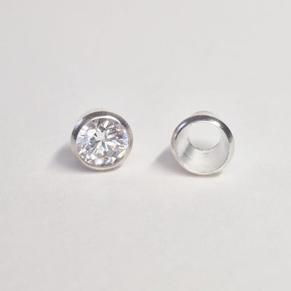 Finished round gemstone set in sterling silver bezel beside empty bezel cup, jewellery setting component on white background.